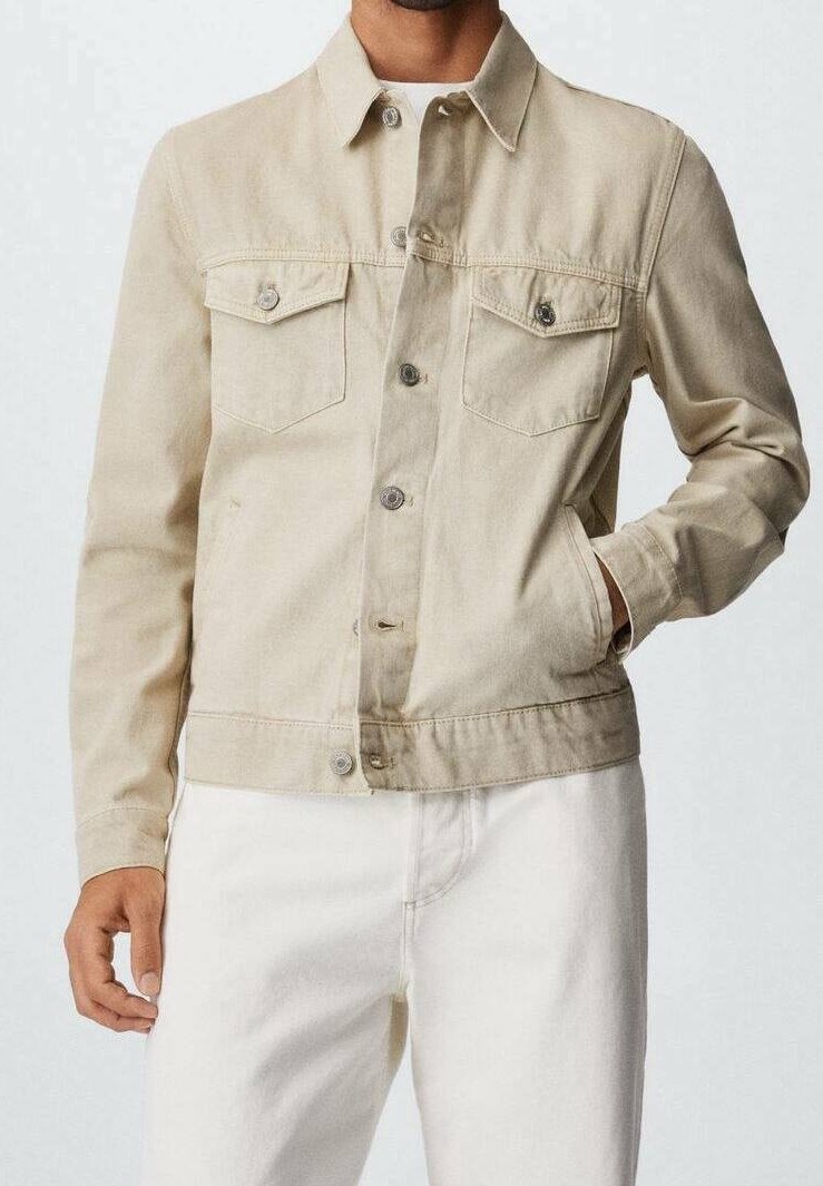 Beige denim takki nappi ylhäältä kahdella rintataskulla, valkoisten housujen päällä, yksi käsi takin taskussa, lyhennetty kaulan ja reiden kohdalla.