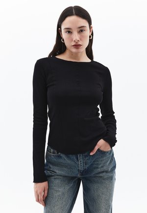 Maglietta a maniche lunghe nera con orlo leggermente curvo, caratterizzata da una texture liscia e dettagli di cucitura minimi. Abbinata a jeans in denim blu.