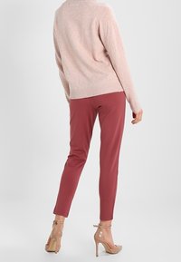 Jasnoróżowy sweter dziergany z ribbowym dołem, zestawiony z dopasowanymi burgundowymi spodniami i przezroczystymi szpilkami, ukazujący gładkie materiały i elegancki design.