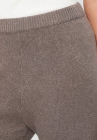 Pantalon de survêtement en tricot marron avec une taille côtelée. Le tissu semble doux avec une texture subtile et un léger éclat. Aucun motif ou accent visible.