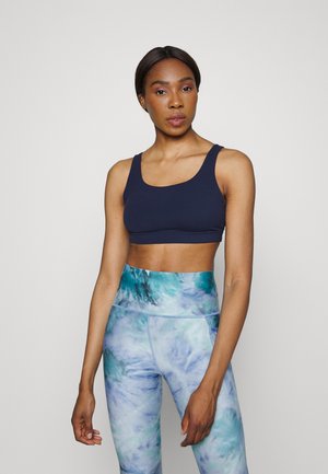 Sutiã desportivo azul-marinho com decote em U combinado com leggings de cintura alta com um padrão de tie-dye em azul e verde.