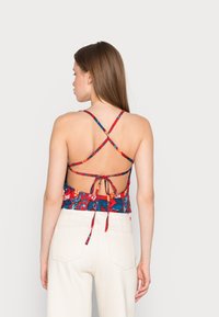 Top corto floreale con un vivace motivo rosso e blu, spalline incrociate, design con schiena scoperta e dettaglio in vita annodato.