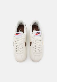 Baskets en cuir blanc avec un logo swoosh marron, lacets plats et col rembourré. La doublure intérieure présente une semelle intérieure marron avec un logo blanc.