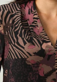 Blouse à motifs avec un mélange de nuances violettes, noires et brunes ; présente des imprimés floraux et animaux ; texture lisse ; col en V.