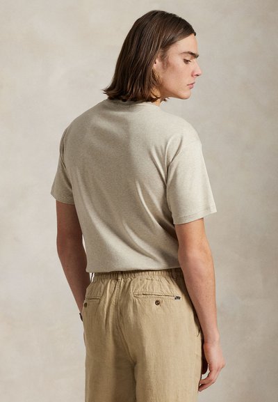 Bež bombažna majica s kratkimi rokavi, zaobljenim izrezom in sproščenim krojem, združena s svetlo bež hlačami z elastičnim pasom in žepi.