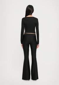 Black long-sleeve crop top and flared pants made of a smooth, stretchy fabric, featuring a simple design and a fitted silhouette.
