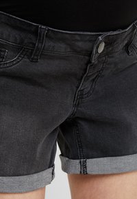 Calções de ganga pretos com barras enroladas. Apresentam um design clássico de cinco bolsos, fecho com botão de metal e detalhes de costura visíveis.
