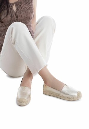 Alpargatas beige metálicas con suelas de yute trenzado, punteras almendradas y diseño sin cordones. Acabado texturizado que realza el interés visual.