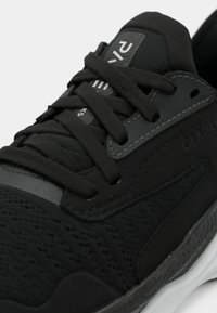 Scarpa da atletica nera con tomaia texturizzata e perforazioni, dettagli lisci e lacci piatti. La suola ha un design di supporto.