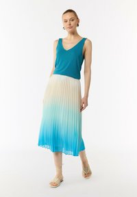 Miętowa bluzka bez rękawów zestawiona z plisowaną spódnicą, która przechodzi od kremowego do jasnoniebieskiego. Modelka nosi beżowe sandały na cienkich paskach.