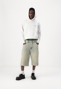 Grå hettegenser, grønne rutete shorts med belte, og svarte klumpete sko. Uformell stil med løse shorts, minimal detaljering.