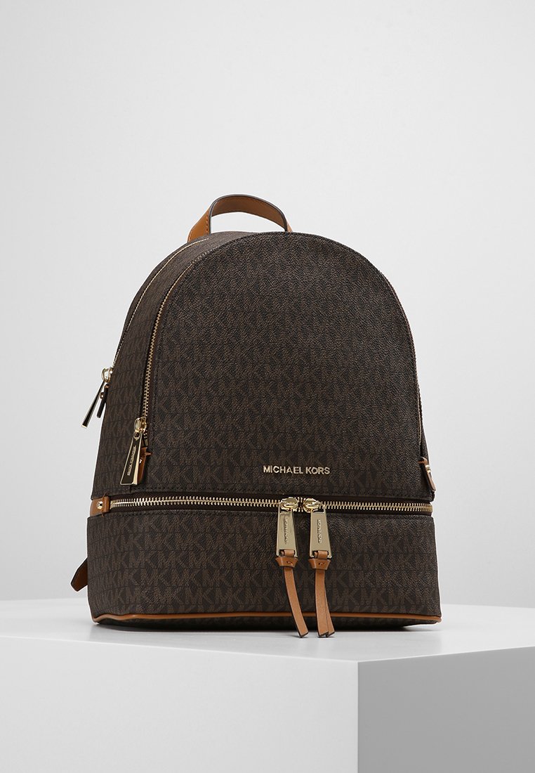 Un sac à dos marron à motifs en matériau texturé, doté de fermetures éclair dorées et d'accents en cuir beige, avec un sommet arrondi et des bretelles doubles.