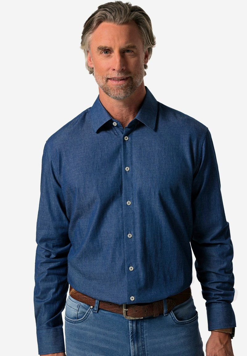 Camicia da uomo a maniche lunghe in tessuto denim blu scuro con colletto, chiusura a bottoni e dettagli in bottoni argentati. Abbinata a jeans chiari.