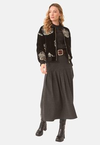 Chaqueta bomber de terciopelo negro con detalles bordados, combinada con una falda negra con estampado. El modelo lleva botas de tacón grueso negras.