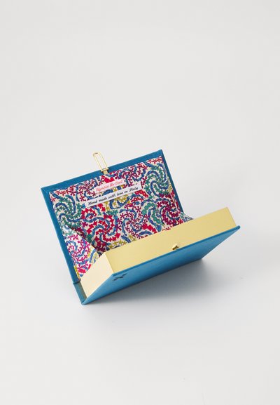 O cutie mică din material albastru cu un închizător aurie, deschisă pentru a dezvălui un interior floral colorat și un etichetă care spune "Confecționată manual cu dragoste în Italia."
