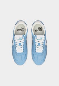 Ζευγάρι από ανοιχτόμπλε αθλητικά παπούτσια Love Moschino με λευκά κορδόνια και μπεζ εσωτερικές σόλες, που φαίνονται από πάνω σε λευκό φόντο.