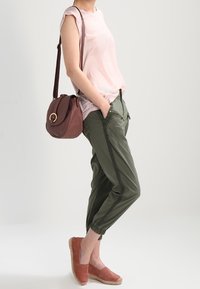 Ljusrosa ärmlös topp, olivgröna joggerbyxor med sidoglidlås, rosa mockaskor och en vinröd axelväska med cirkulär detalj.