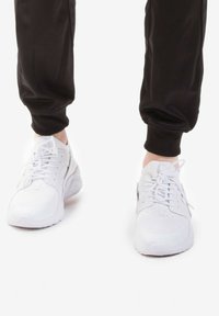 Le scarpe da ginnastica bianche hanno un upper in rete testurizzata, un design con lacci e una suola imbottita, abbinate a joggers neri a gamba affusolata.