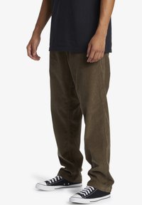 Corduroy pants in dark olive green with a straight leg design, featuring a soft texture and worn with black canvas sneakers.