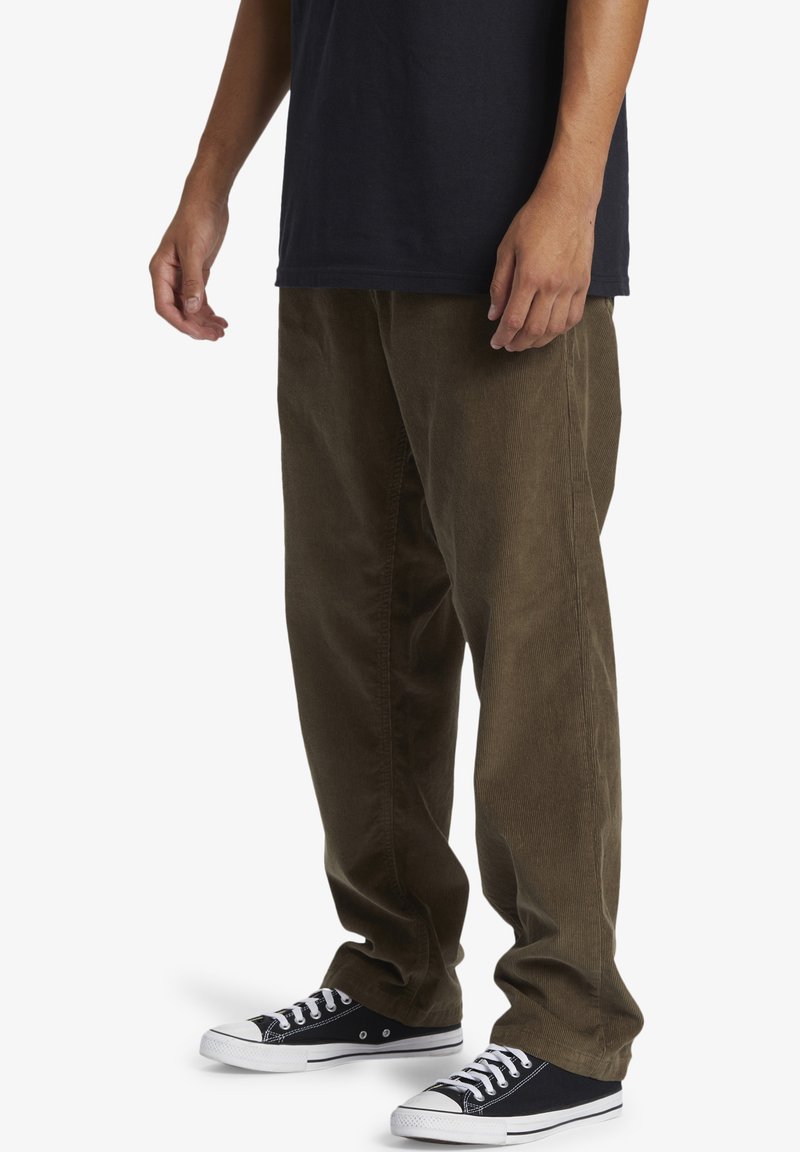 Corduroy pants in dark olive green with a straight leg design, featuring a soft texture and worn with black canvas sneakers.