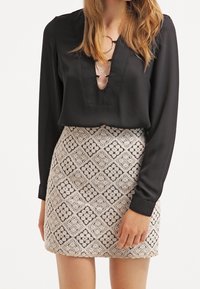 Blusa nera a maniche lunghe con scollo a V e ritagli circolari, abbinata a una gonna beige chiaro texturizzata con un motivo geometrico nero.