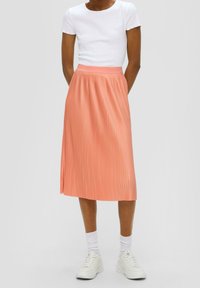 Falda midi plisada en suave coral, confeccionada con tela ligera. Cuenta con cintura alta y una superficie lisa y texturizada, combinada con una blusa blanca.