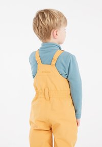 Gula vattentäta overaller med justerbara remmar, elastisk midja, tillsammans med en teal fleece-tröja. Enkel design, inga synliga mönster.