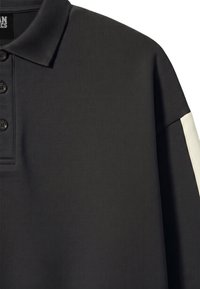 Polo noir à manches longues avec un col, trois boutons sur le devant et une bande blanche sur la partie supérieure de la manche.