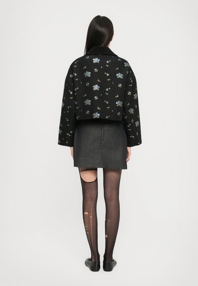 Μαύρο κοντό μπουφάν με λουλουδάτα κεντήματα, γκρι φούστα και μαύρες κολάν με αρκετές μεγάλες κοπές. Οι επίπεδες μαύρες γόβες ολοκληρώνουν την εμφάνιση.