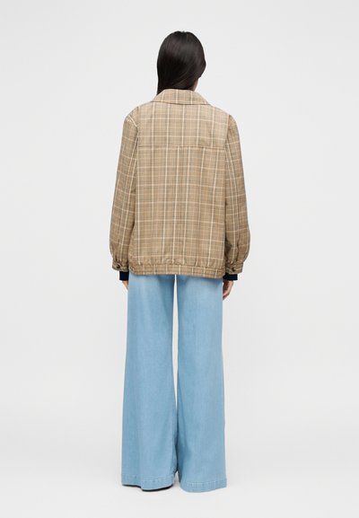 Καφέ καρό σακάκι σε υπερμέγεθος με φουσκωτά μανίκια, ελαστική μέση και αντίθετο μπλε τζιν παντελόνι με φαρδιά μπατζάκια. Απλός σχεδιασμός, χωρίς επιπλέον διακοσμητικά.