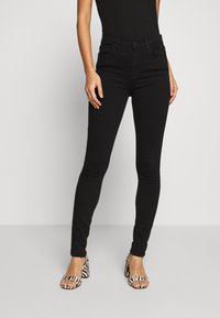 Zwarte skinny jeans van denim, met een hoge taille, vijf zakken en een gladde textuur, gecombineerd met zwart-wit gestreepte hoge hakken sandalen.