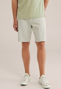 Hellgrüne Baumwollshorts mit lockerer Passform, ausgestattet mit Seitentaschen und genähten Säumen. Getragen mit weißen Sneakern und einem hellgrünen Oberteil.