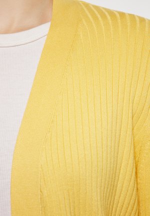 Žlutý žebrovaný kardigan s texturovanou tkaninou a otevřeným předním designem, nošený přes světle růžový obtáhlý top.