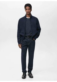 Giacca zip navy sopra una maglietta navy, abbinata a jeans in denim scuro e scarpe nere stringate. Tessuto morbido con una vestibilità rilassata.