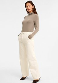 Beige långärmad topp med hög hals, matchad med vida crèmefärgade corduroybyxor och bruna klackskor. Enkel och minimalistisk design.