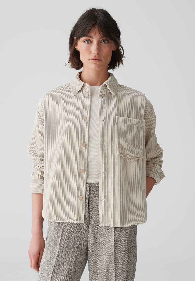 Beige corduroy shirt with vertical stripes, button closure, collar, and single chest pocket. Long sleeves with rolled cuffs.