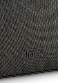 Bolsa de tela negra con superficie texturizada y logotipo en relieve. El material presenta un patrón sutil para mayor detalle.