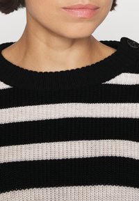 Sweter w paski z czarnymi i beżowymi poziomymi paskami, żebrowana tekstura, okrągły dekolt oraz zapięcie na guzik na ramieniu.