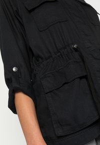 Sort letvægtsjakke med oprullede ærmer, justerbar talje snor og to frontlommer. Glat tekstur og holdbart stof.