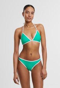 Zeleni bikini z belimi robovi; trikotni zgornji del in nizko pasu; gladka tekstura tkanine; minimalističen dizajn.