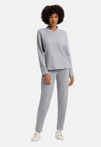 Lichtgrijze lounge set gemaakt van zachte stof, met een lange mouw V-hals top en bijpassende taps toegesneden broek, gecombineerd met witte sneakers.