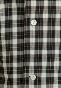 Hemd mit Knöpfen, das ein schwarz-weiß-tan kariertes Muster aufweist, mit glatter Textur und einem weißen Knopf in der Mitte.
