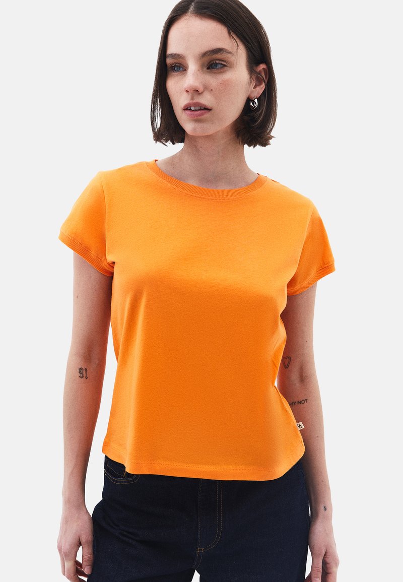Tee s krátkým rukávem v oranžové barvě, vyrobená z hladké tkaniny, s kulatým výstřihem a volným střihem. Čistý design bez viditelných vzorů nebo potisků.