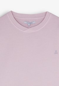 T-shirt en coton rose clair avec un col en V et un petit logo de skull brodé en gris, affichant une texture douce et un design simple.