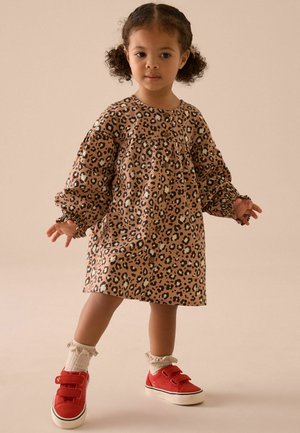 Leopardenmuster-Kleid in Beige und Braun, mit langen Puffärmeln und geraffter Taille. Kombiniert mit roten Schuhen und weißen Rüschen-Socken.
