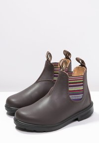 Hnědé kožené kotníkové boty s elastickými bočními panely a barevnými pruhy. Pevná podrážka s dezénem pro lepší přilnutí a poutka pro snadné obouvání.