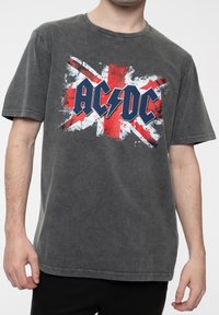 Gray cotton T-shirt featuring an AC/DC graphic with a distressed Union Jack background in red and white. Short sleeves and a crew neck design.