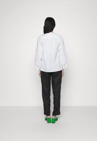 Camicetta bianca con maniche a sbuffo, abbinata a pantaloni neri e scarpe con tacco a blocco verdi. Tessuto liscio e design semplice.
