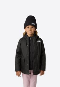 Černá nepromokavá bunda s kapucí, zapínáním na zip a patentkami. Nositá přes černou vnitřní vrstvu, doplněná o růžové kalhoty a černou čepici.