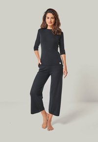 Schwarzes Strickoberteil mit dreiviertelÄrmeln, kombiniert mit weit geschnittenen schwarzen Hosen, die beide ein strukturiertes Design und ein kleines Logotag aufweisen.
